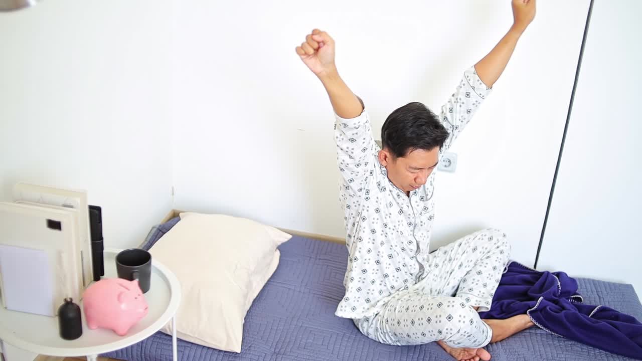 Young Man in pajamas waking up and stretching in bedroom feeling refreshed and energized for day