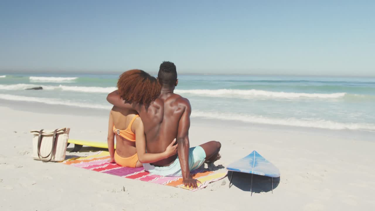 una pareja afroamericana acurrucada en la playa.