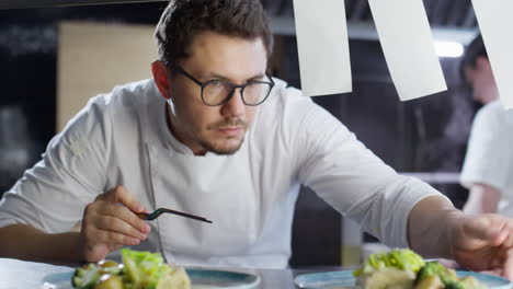 male chef serving dishes with tweezers in restaurant kitchen