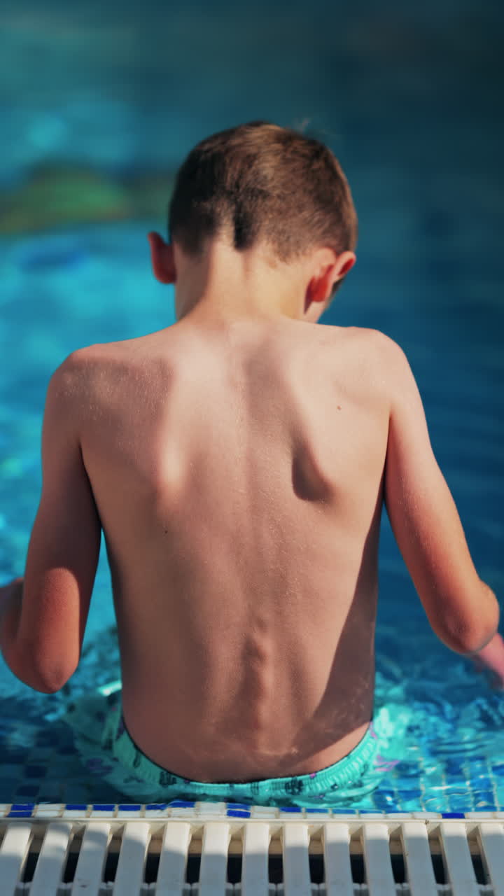 Overhead shot of a young boy playing in a bright blue swimming pool. Vertical