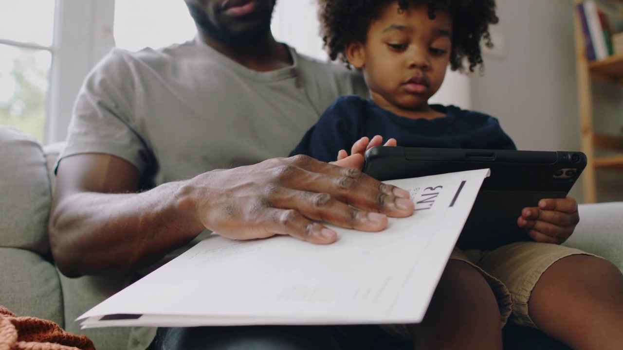 Smoothing parent steadying mail on sofa after child settling on lap, child holding tablet