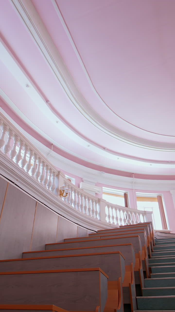 Empty auditorium at university. Large classroom with rows of wooden desks without students. Steps among tables in the large lecture hall. Pandemic. Vertical video