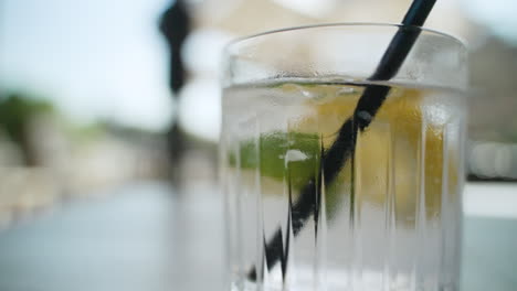 hand lets go of a straw after mixing glass with water, lemon wedge, lime, and ice cubes