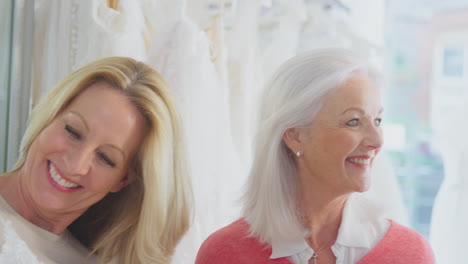 grandmother with adult granddaughter watching mother choosing wedding dress in bridal store