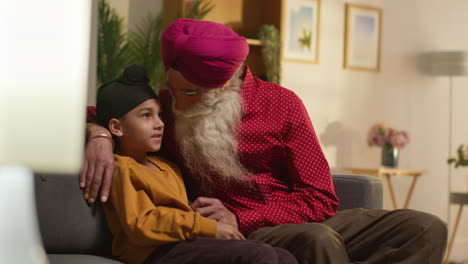 grand-père et petit-fils sikhs souriants portant des turbans assis sur le canapé à la maison en train de parler ensemble 3