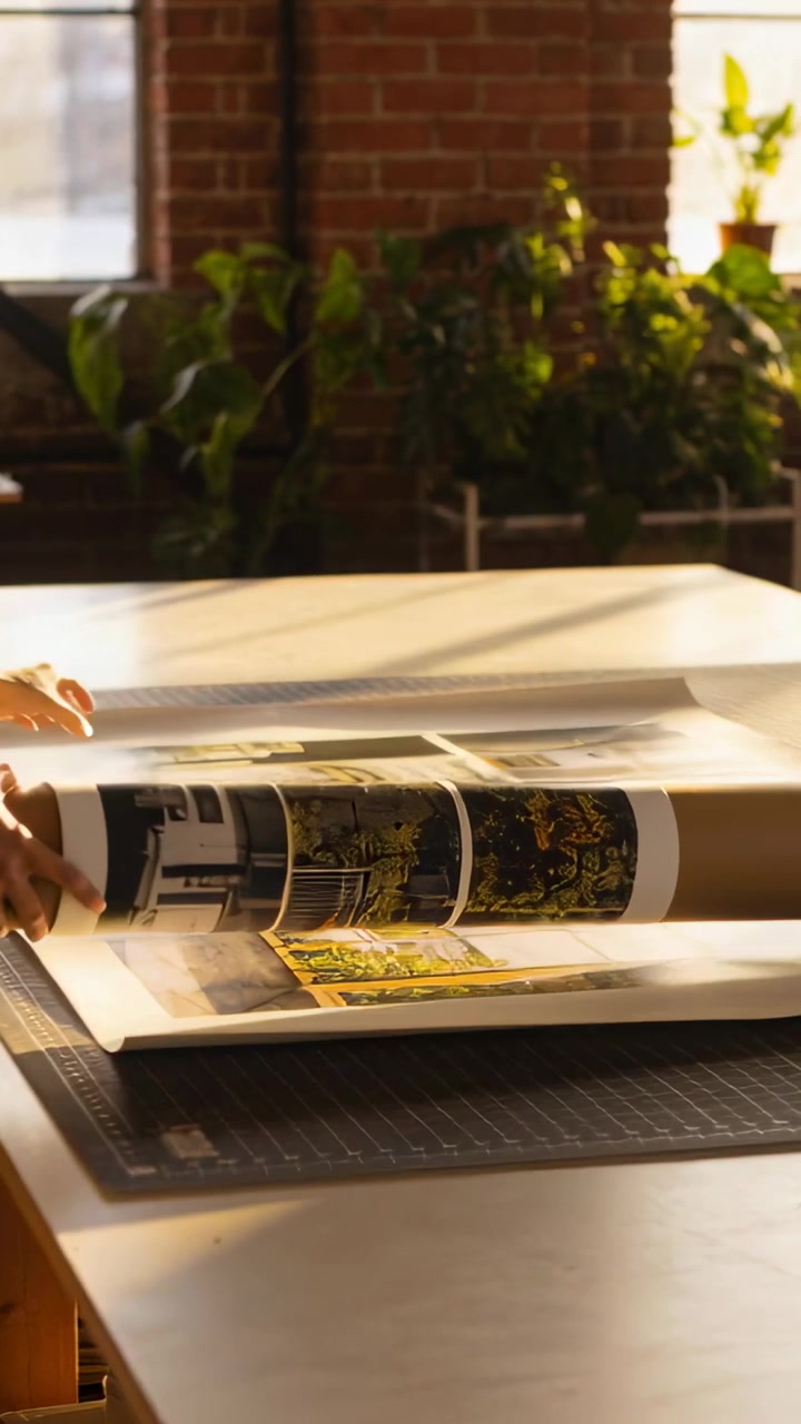 Vertical video: Reaching from left, sleeved arms unrolling roll over prints in studio for storage