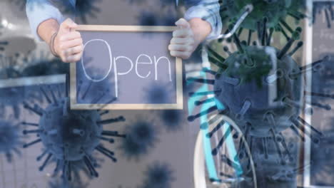 animation of macro covid-19 cells floating over caucasian woman holding an open sign