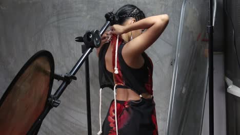 bastante joven modelo asiática vistiéndose frente al espejo para una sesión de fotos dentro de un estudio desnudo con el reflector del estudio en el fondo