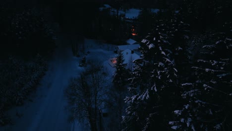 aerial view around snowy trees, revealing a illuminated house, dark, winter evening