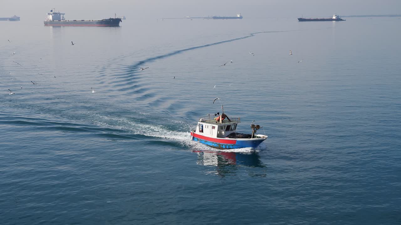 Fishing boat in front of large industrial vessels in harbour of Taranto, Italy in nice sunny day