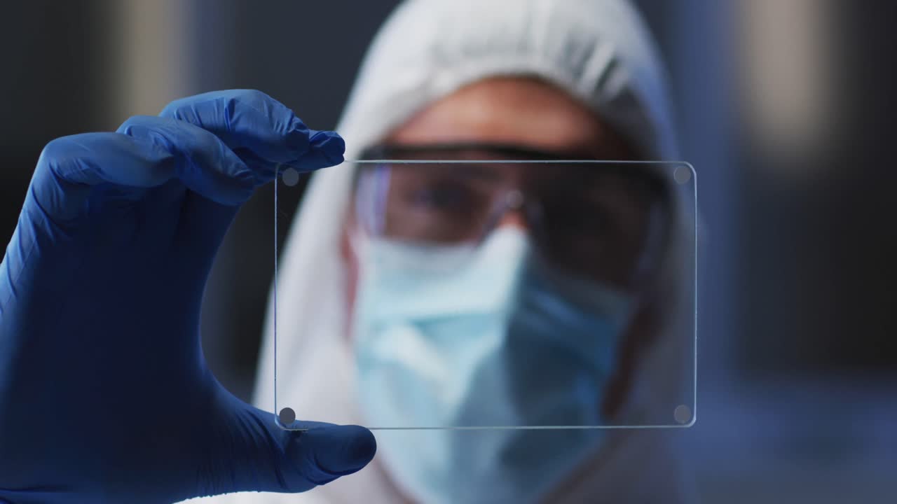 Caucasian male medical worker wearing protective clothing and gloves using handheld interface in lab