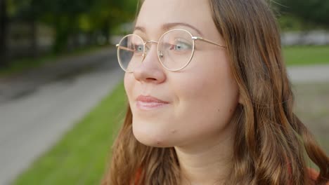 primer plano, mujer bonita poniendo nuevas gafas ópticas en el parque, cámara lenta