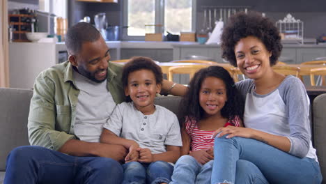 Portrait-Of-Family-On-Sofa-In-Open-Plan-Laughing-Towards-Camera