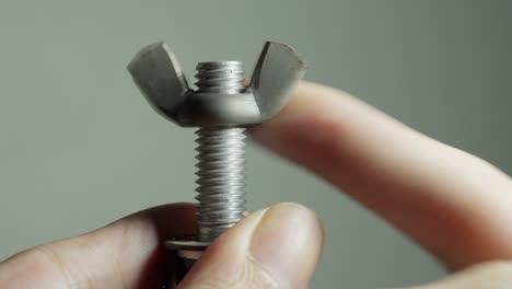 turning and fasten a steel wing bolt screw by hand and finger, close up