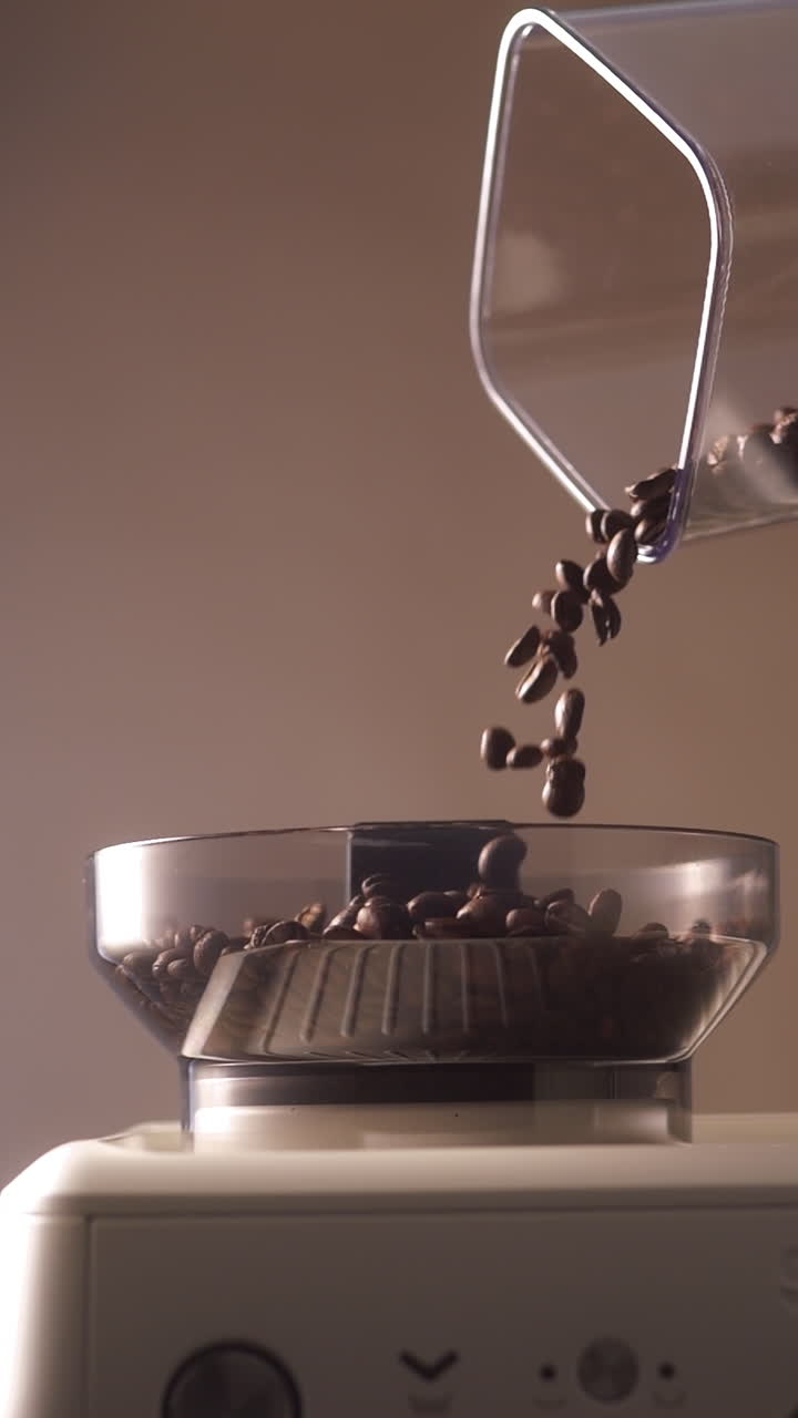 Rallentatore cinematografico di chicchi di caffè tostati che cadono nel contenitore del macinino di una macchina da caffè espresso professionale. Una luce morbida e calda enfatizza il movimento, la texture e il processo di preparazione