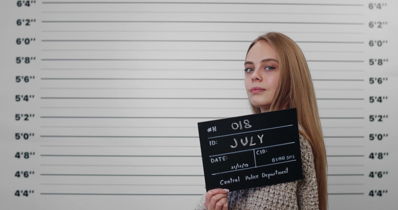 Giovane donna che tiene un cartello da foto segnaletica davanti a uno sfondo da riconoscimento della polizia