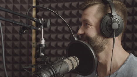 a radio presenter with a beard speaks through the microphone in a radio studio