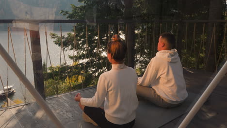 couple practicing yoga meditation on a balcony with a lake view