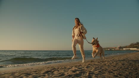 Jogging-and-playing-with-her-pets-a-blonde-girl-on-the-beach-runs-with-her-big-gray-dog-in-the-morning