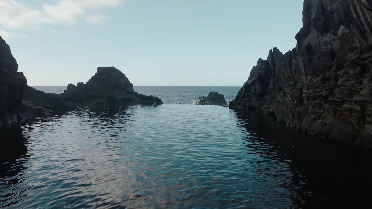 View from inside a volcanic cave framing the natural pools and Atlantic Ocean in Seixal, Madeira during calm daylight.