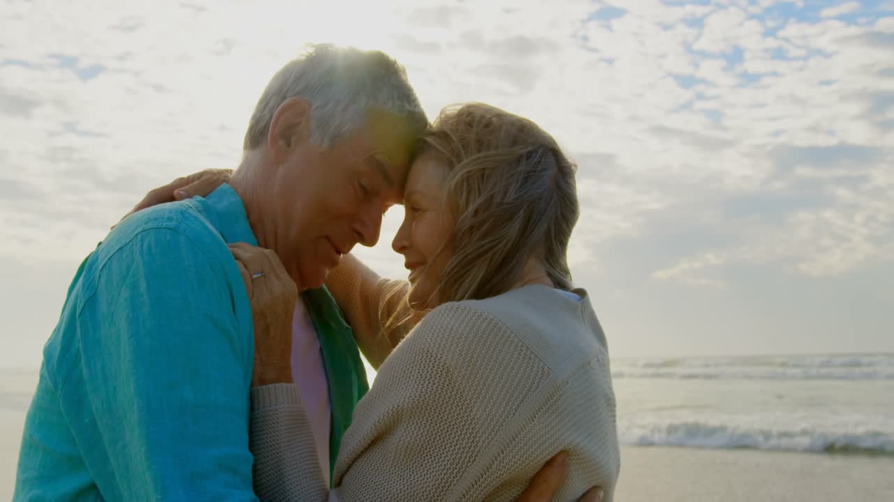vista lateral de una pareja caucásica senior activa abrazándose en la playa 4k