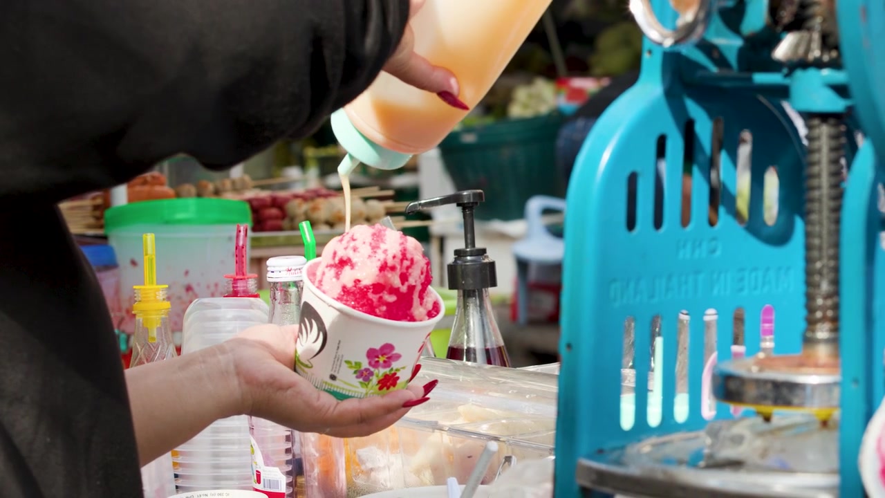 Venditore ambulante che prepara un dessert di ghiaccio tritato in un mercato all'aperto.