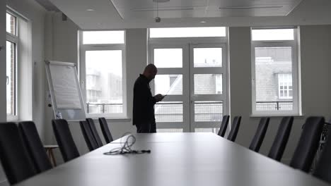 an individual strides through an office conference room, passing by a lengthy table encircled by chairs, symbolizing the essence of a corporate gathering or similar professional rendezvous