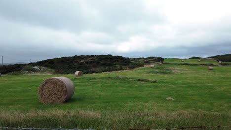 prado de campo húmedo con balas de heno de paja enrollada en tierras de cultivo británicas nubladas abiertas