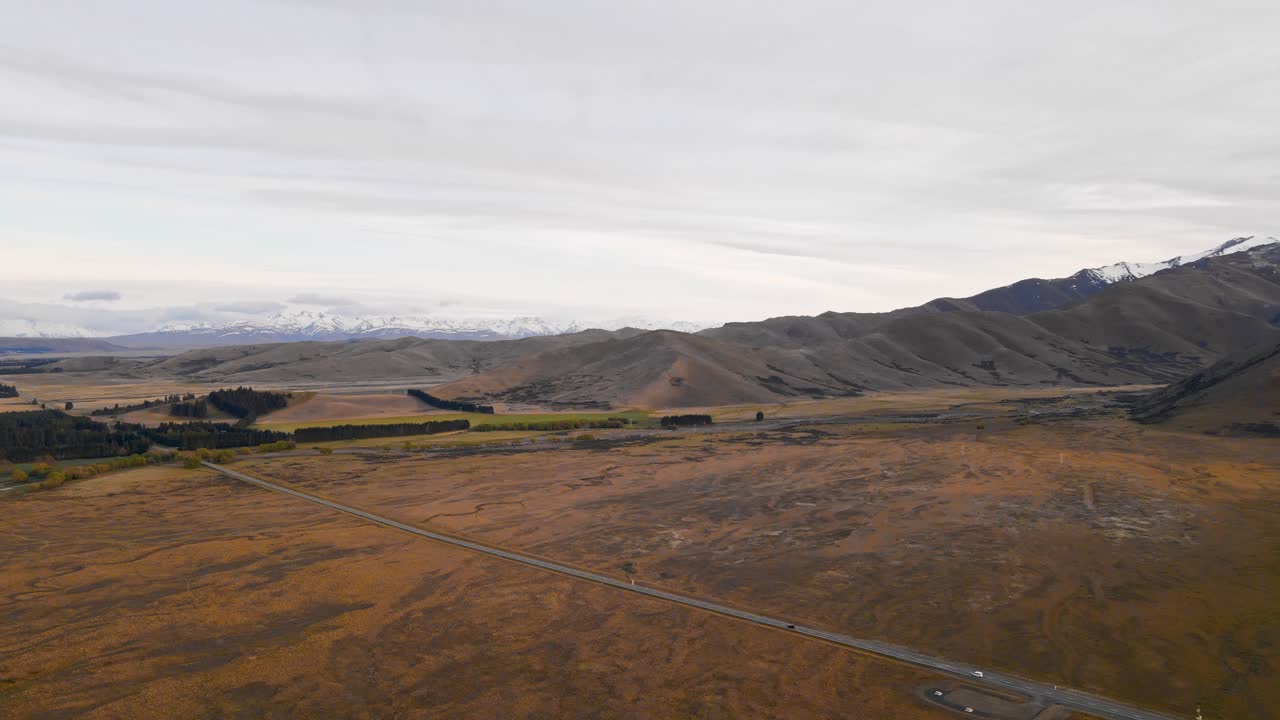 панорамный вид с воздуха, отслеживающий движение двух автомобилей по сельскому шоссе, ведущему к живописному горному хребту