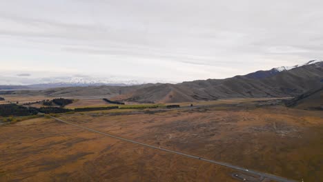 panning aerial view tracking two cars driving along a rural highway that leads towards a picturesque mountain range