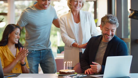 Staff-Celebrating-Birthday-Of-Male-Colleague-At-Desk-In-Office-With-Cake