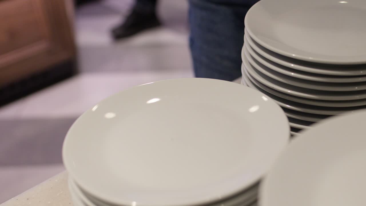 Close-up of person arranging clean white plates on buffet counter in warm restaurant lighting