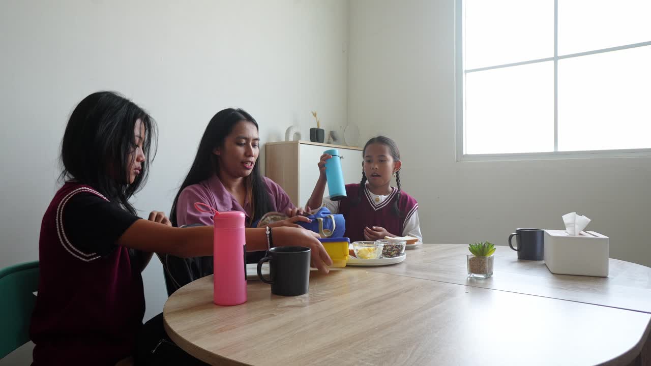 Madre asiatica che prepara il pranzo al sacco e la borraccia per sua figlia prima di andare a scuola