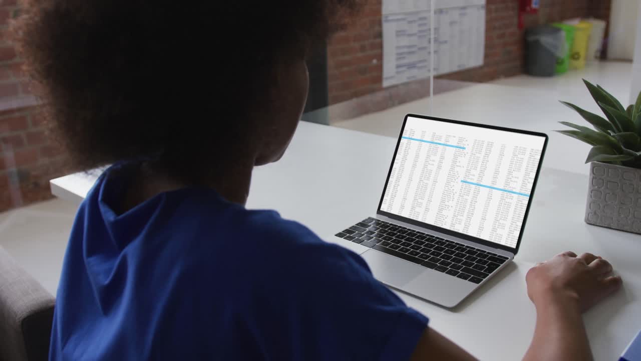 African american woman sitting at desk watching coding data processing on laptop screen