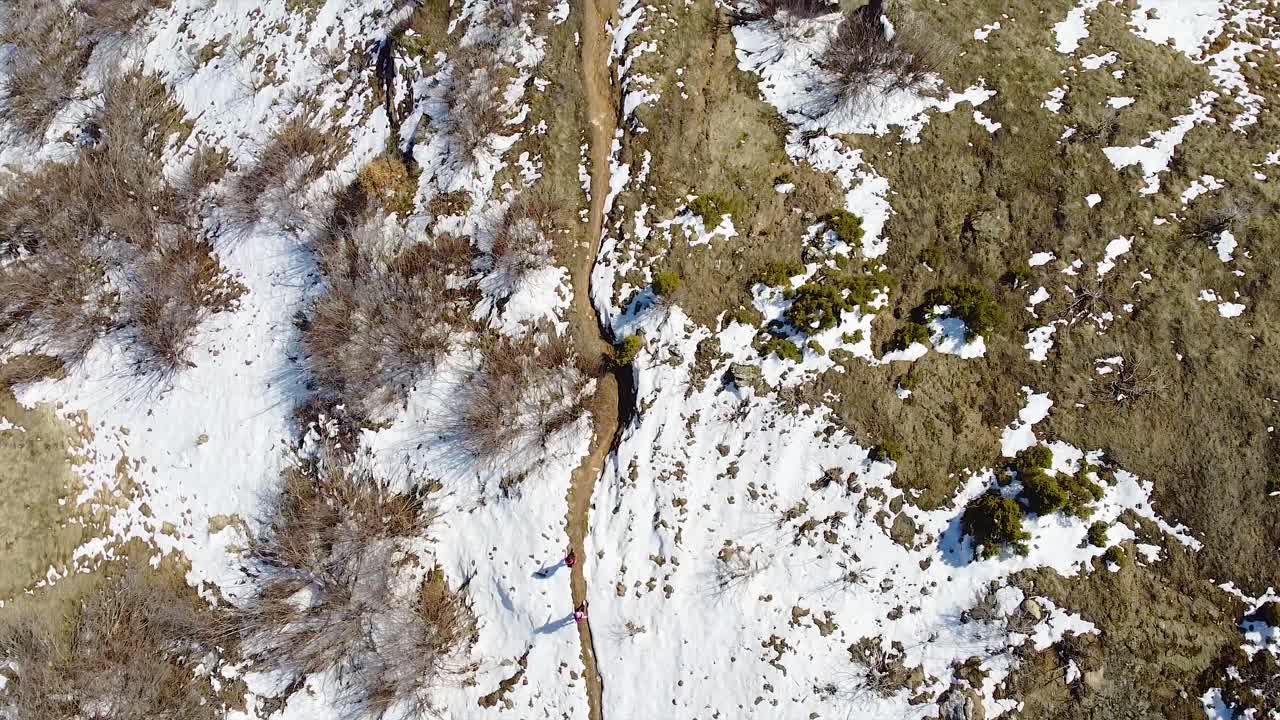 Hikers hiking on a small mountain path covered in snow in winter drone shot
