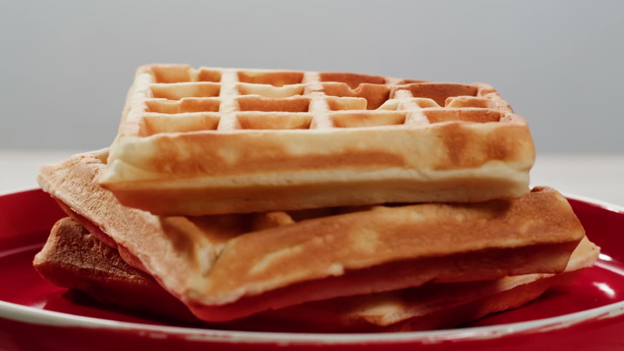 신선하게 조리 된 황금 와플의 아름답게 배열 된 클로즈업, 능숙하게 활기찬 빨간 접시에 높게 쌓여