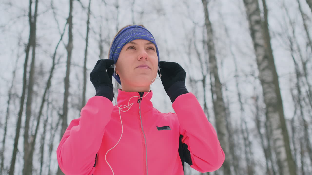 The woman before the morning winter jog inserts headphones in the ears and is preparing to run through the natural Park in slow motion.