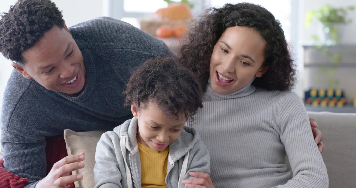 Famiglia afroamericana sul divano che guarda un tablet, bambino che tocca, adulti che reagiscono allo schermo.