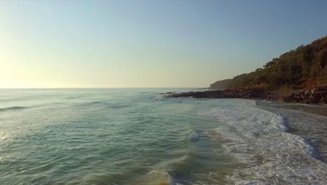 Aerial-drone-shot-low-over-the-ocean-towards-fisherman-on-rocks