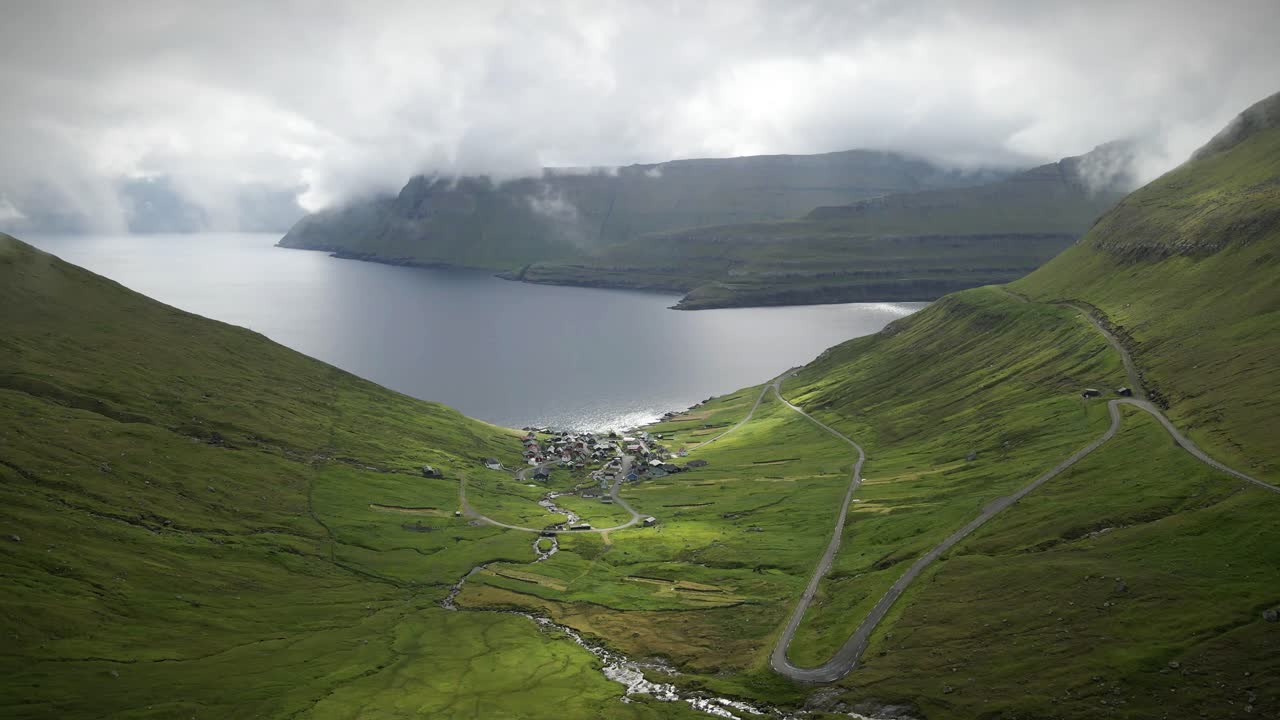 푸른 언덕, 휘어지는 도로, 조용한 피오르드, 그리고 덴마크 페로 제도의 닝스피오르드 (funningsfjord) 에 있는 극적인 구름의 구링 마을은 숨막히는 북유럽 풍경 드론  촬영을 만니다.