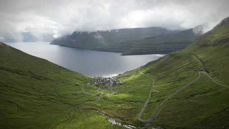 green hills, winding roads, a serene fjord, and dramatic clouds of funningur village on the funningsfjord in the faroe islands, denmark, creating a breathtaking nordic landscape drone panning shot