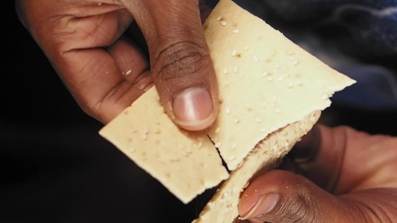Person Holding and Breaking Sesame Crackers