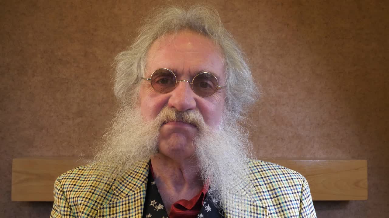 un hombre mayor con barba se pone gafas y nodos ante la cámara