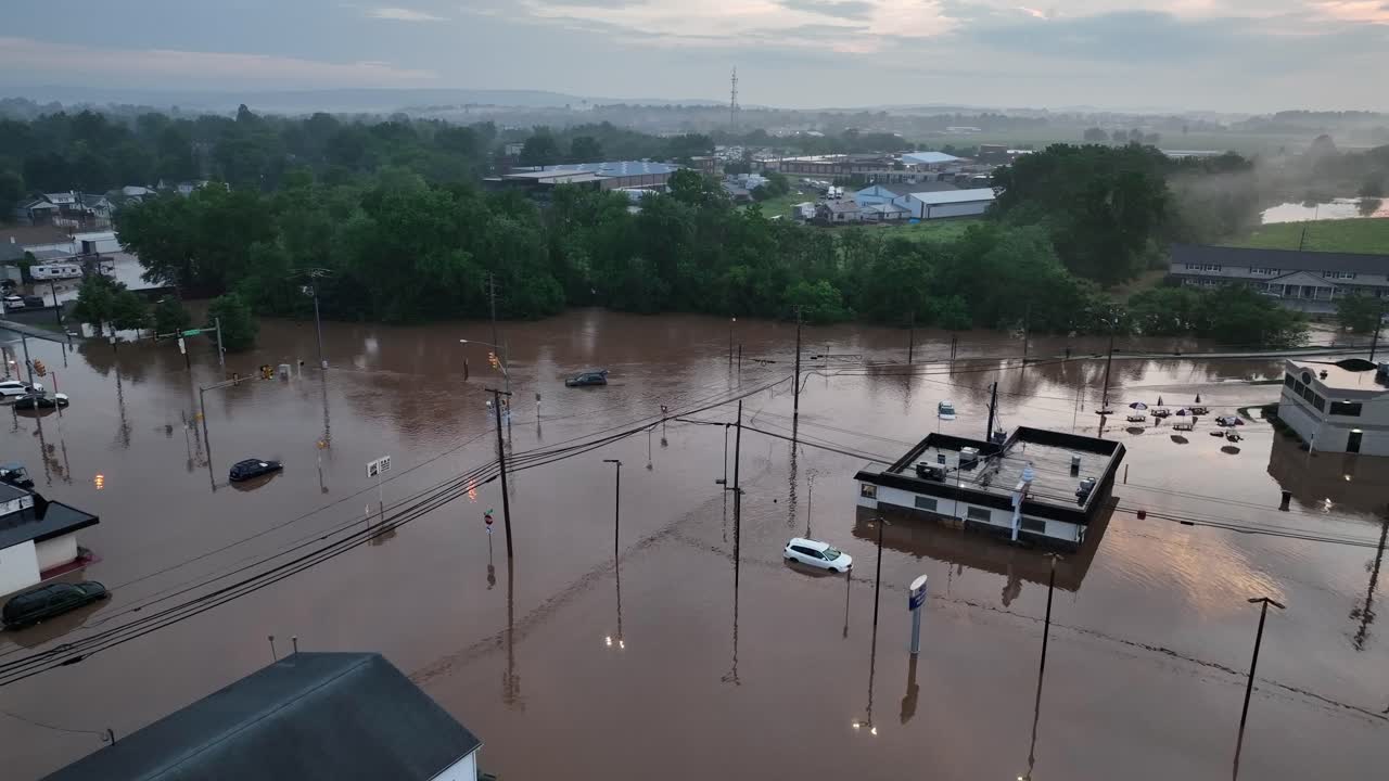 Flood river stream covering streets and roads in small town America, USA. Aerial drone wide shot at golden hour morning sunrise. Flooded houses and buildings after rainfall