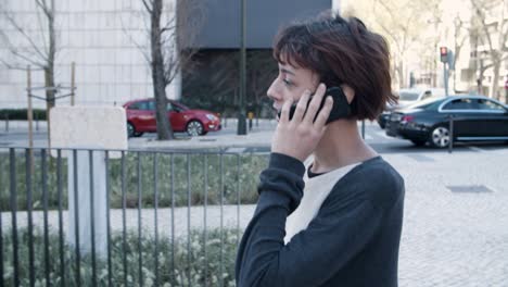 Side-view-of-calm-woman-walking-and-talking-on-smartphone