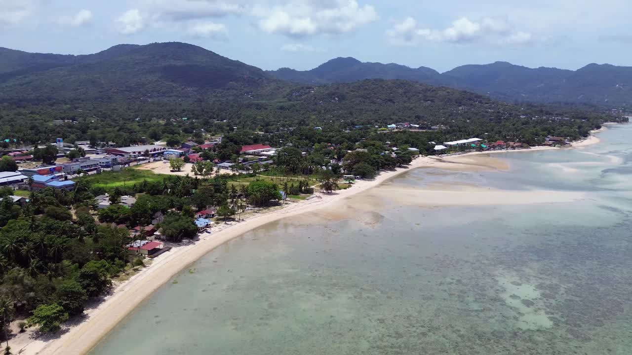 Aerial footage of Thong Sala Beach with a wide sandy shoreline, turquoise sea and lush tropical scenery on Koh Phangan island, Thailand