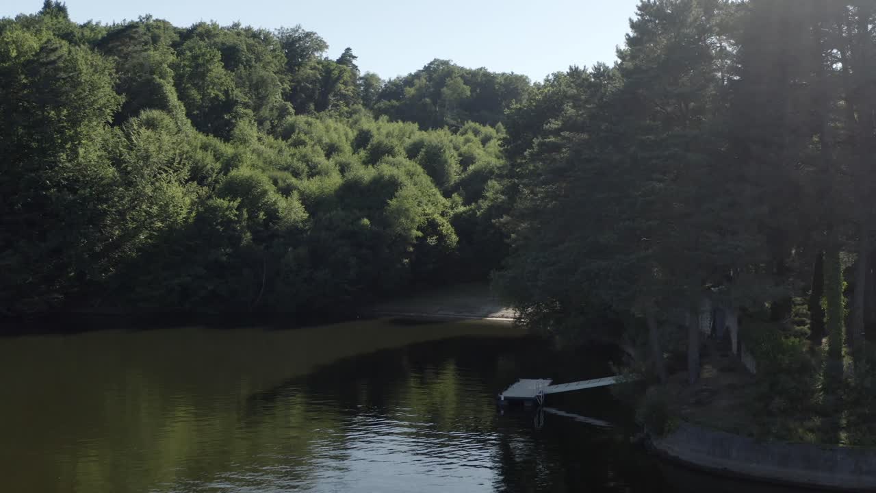 Aerial view of secluded wooden dock on calm lake surrounded by dense green forest, Marcillac La Croisille, France