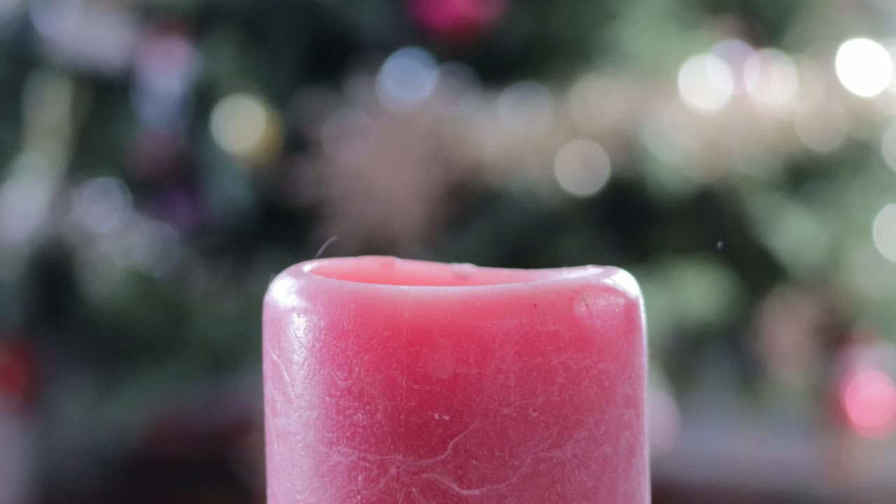 Una candela rosso acceso accesa di fronte a un albero di Natale decorato