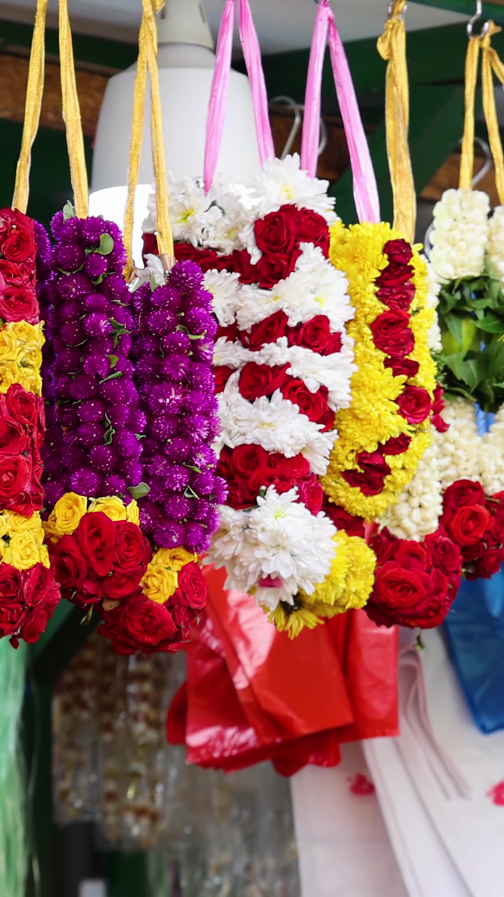 Ghirlande di fiori vivaci fatte di rose, crisantemi e calendule appese in file in una bancarella del mercato a Singapore. Illuminazione naturale brillante, fluida panoramica laterale della telecamera.