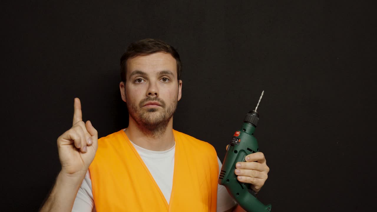 A worker in a reflective vest holds a drill and raises his finger in warning, emphasizing the importance of wearing safety glasses to protect the eyes during work